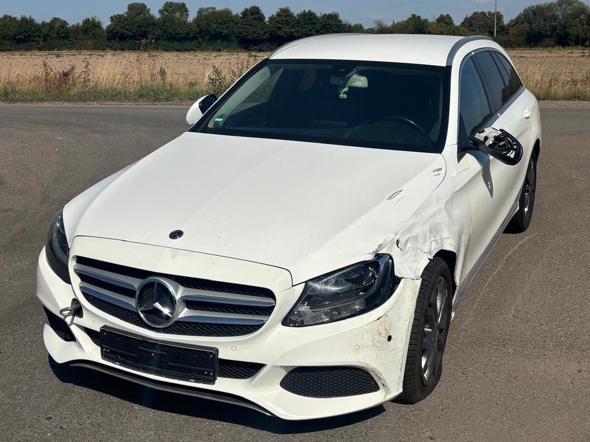 Unfallfahrzeug mit Frontschaden auf dem Betriebshof: weißer Mercedes-Kombi mit eingedrückter Stoßstange und beschädigtem Kotflügel