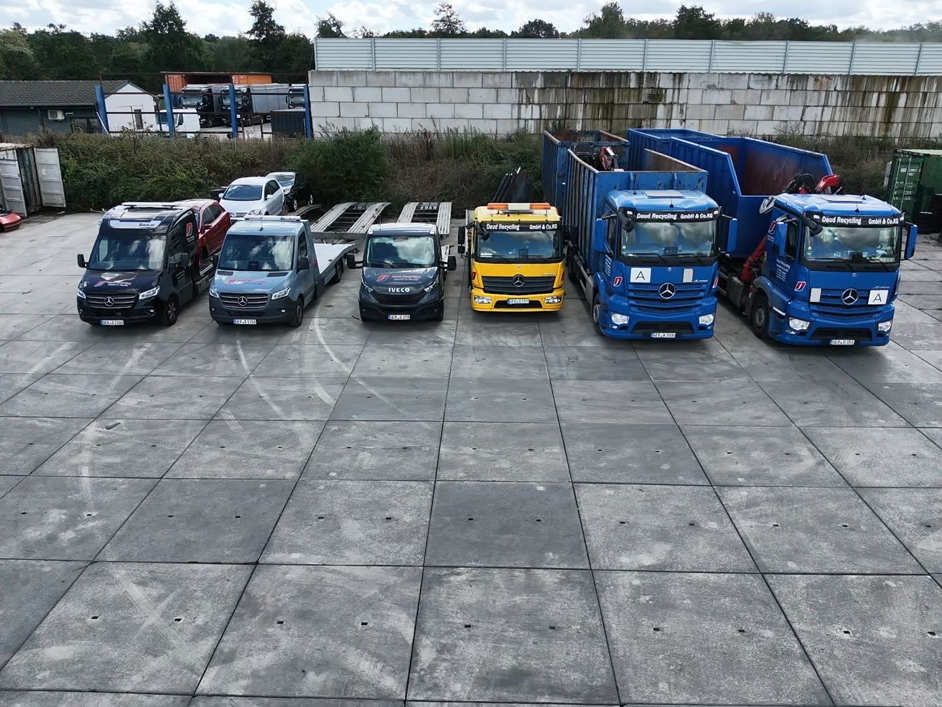 Die Fahrzeugflotte von oben: Sprinter mit Anhängern, Abschleppwagen und zwei Lkw mit Abrollcontainern auf dem Betriebshof