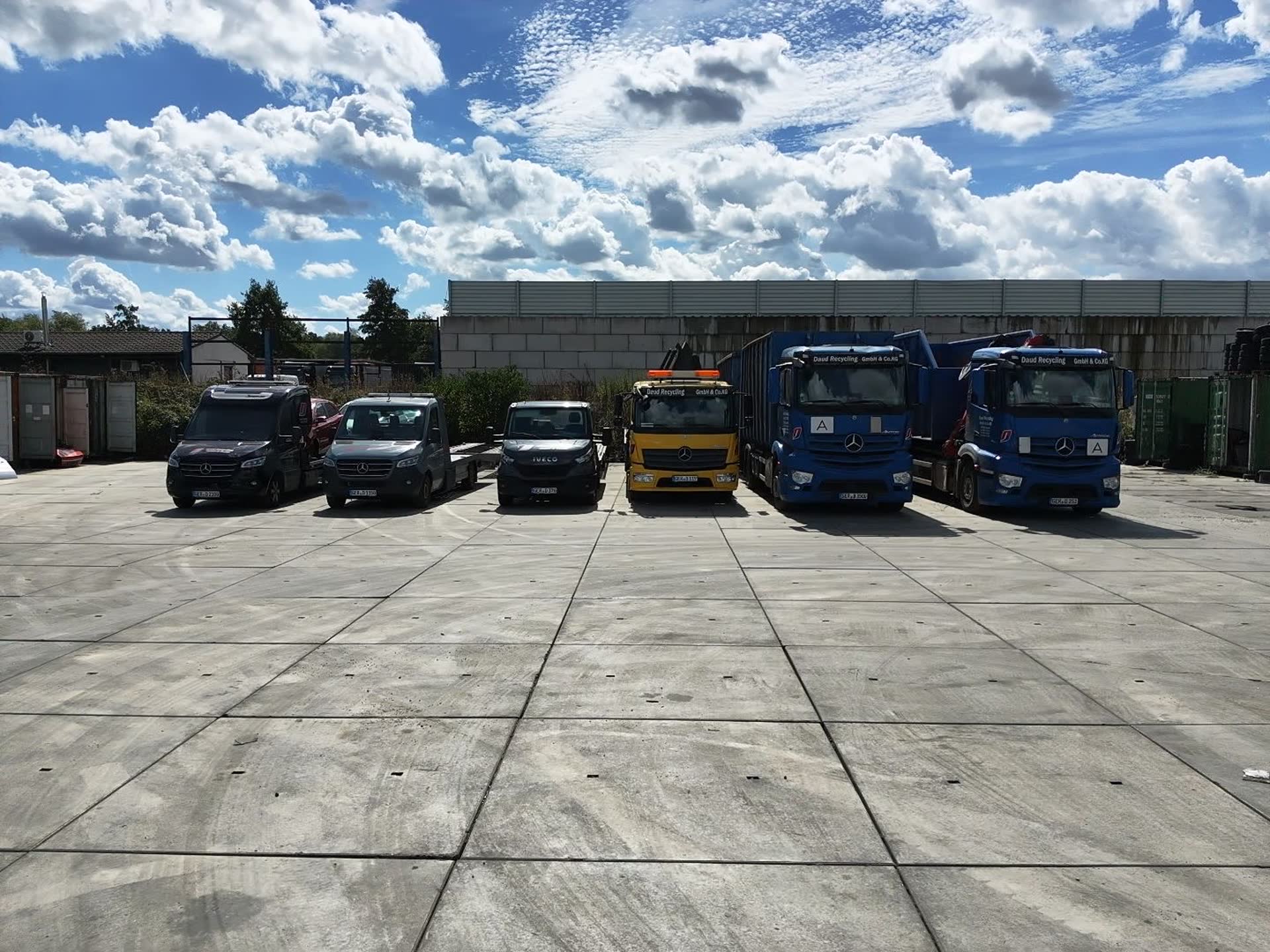 Die Fahrzeugflotte von Daud Recycling nebeneinander auf dem Betriebshof: Sprinter mit Anhängern, Abschleppwagen und zwei Lkw mit Abrollcontainern